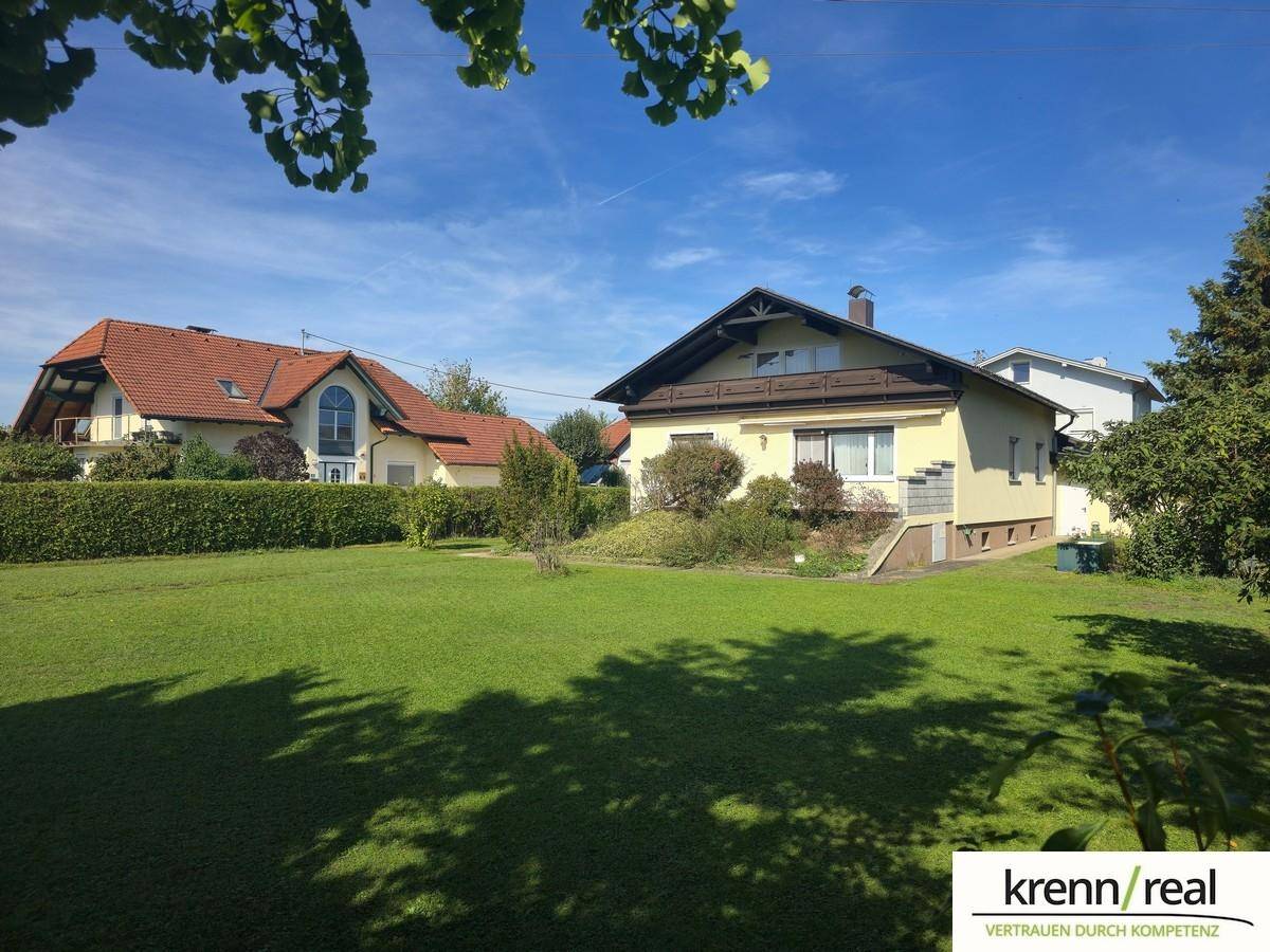 Großzügiger Gartenbereich neben dem Einfamilienhaus mit viel Grünfläche und Hecken unter strahlendem Himmel.