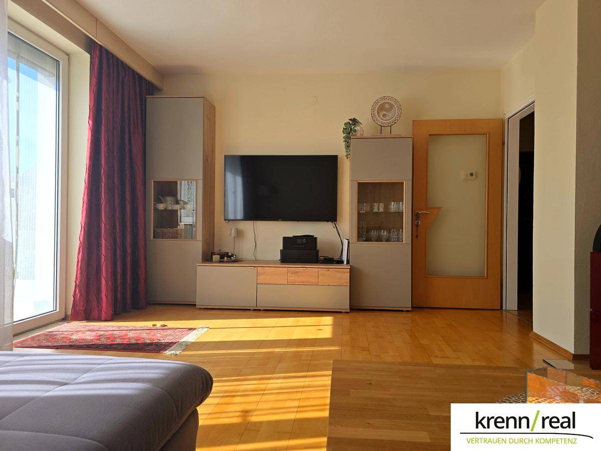 Helles Wohnzimmer mit Holzparkett, modernen Möbeln und Zugang zu einem sonnigen Balkon.