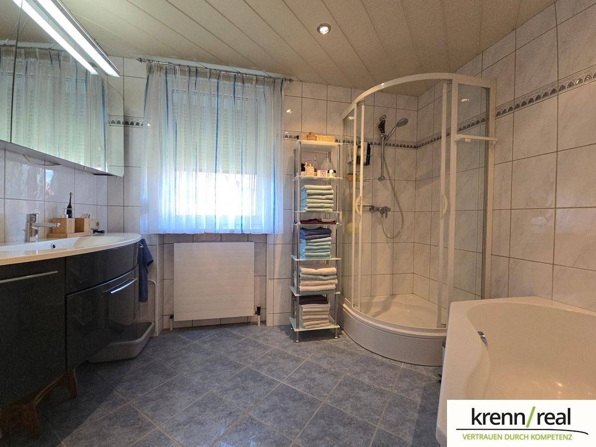 Gefliestes Badezimmer mit Duschkabine, Badewanne und Fenster für natürliche Belüftung und Licht.
