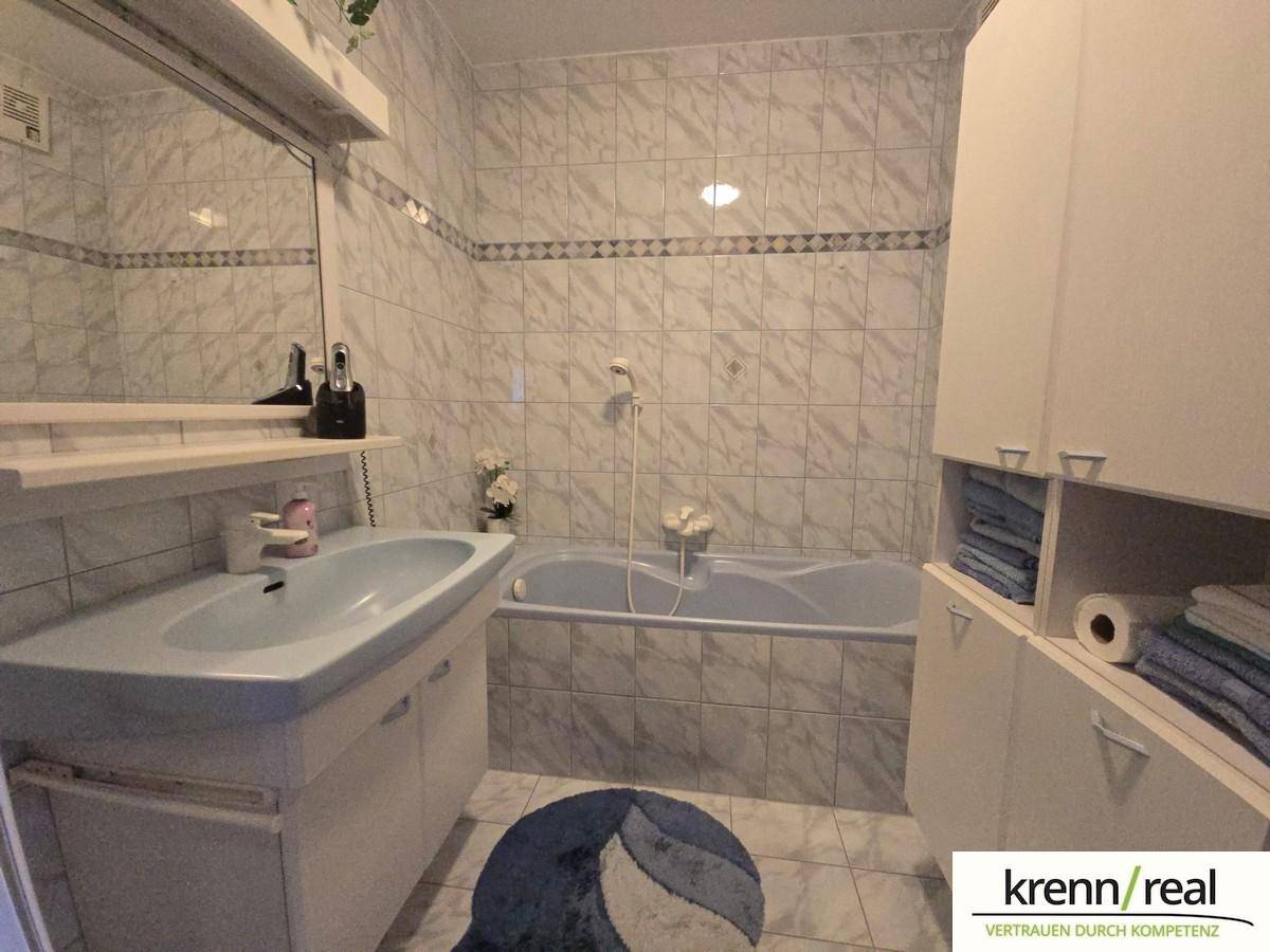Gefliestes Badezimmer mit Badewanne, Waschbecken und praktischen Stauschränken.