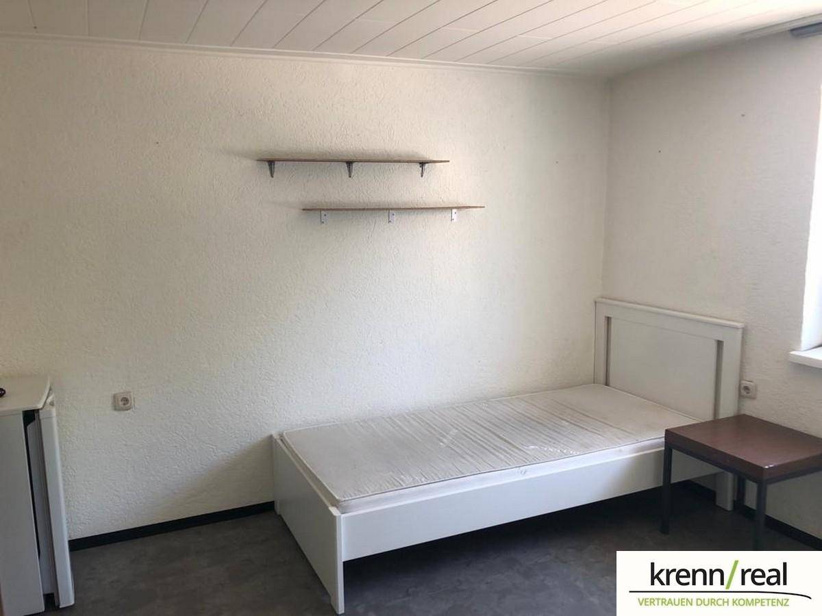 Einfaches Schlafzimmer mit Einzelbett, zwei Wandregalen und einem kleinen Beistelltisch.