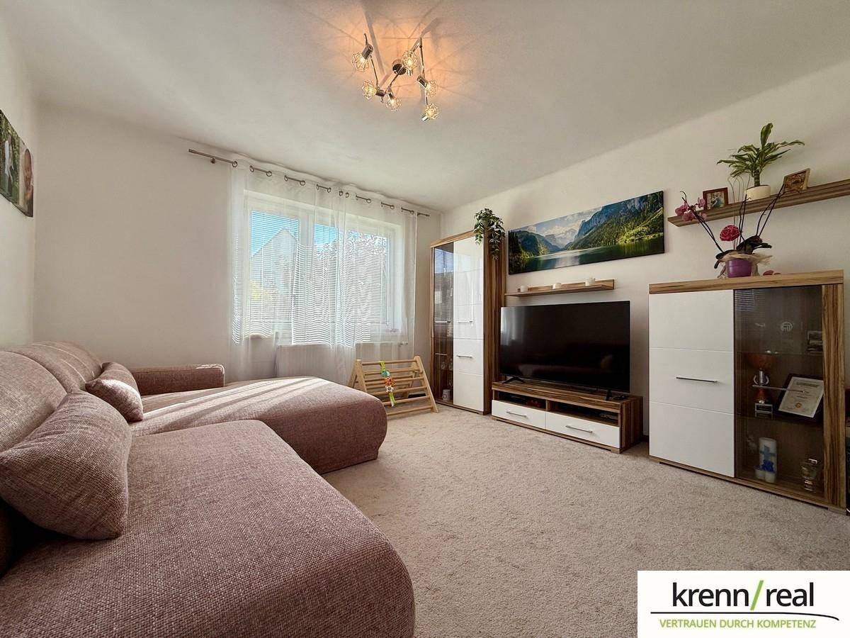 Gemütliches Wohnzimmer mit großem Sofa, Teppichboden und Blick ins Grüne.