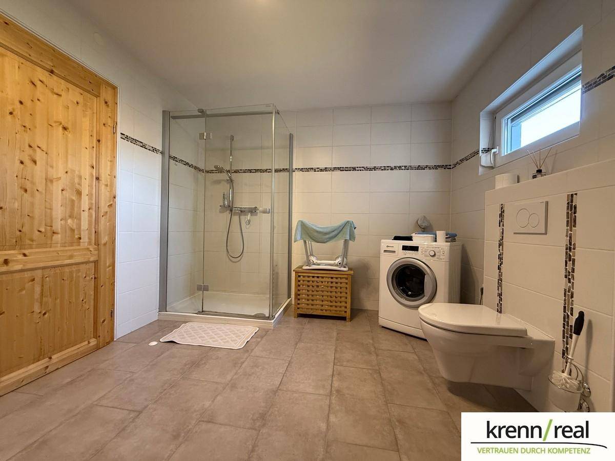 Geräumiges Badezimmer mit ebenerdiger Dusche, Toilette, Waschmaschine und Fenster.