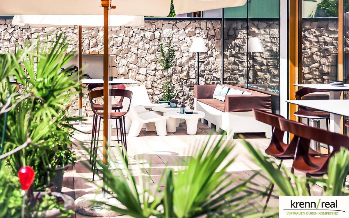 Gemütlicher Außenbereich mit Lounge-Möbeln, einer Steinwand und üppiger Bepflanzung, ideal zum Entspannen im Freien.