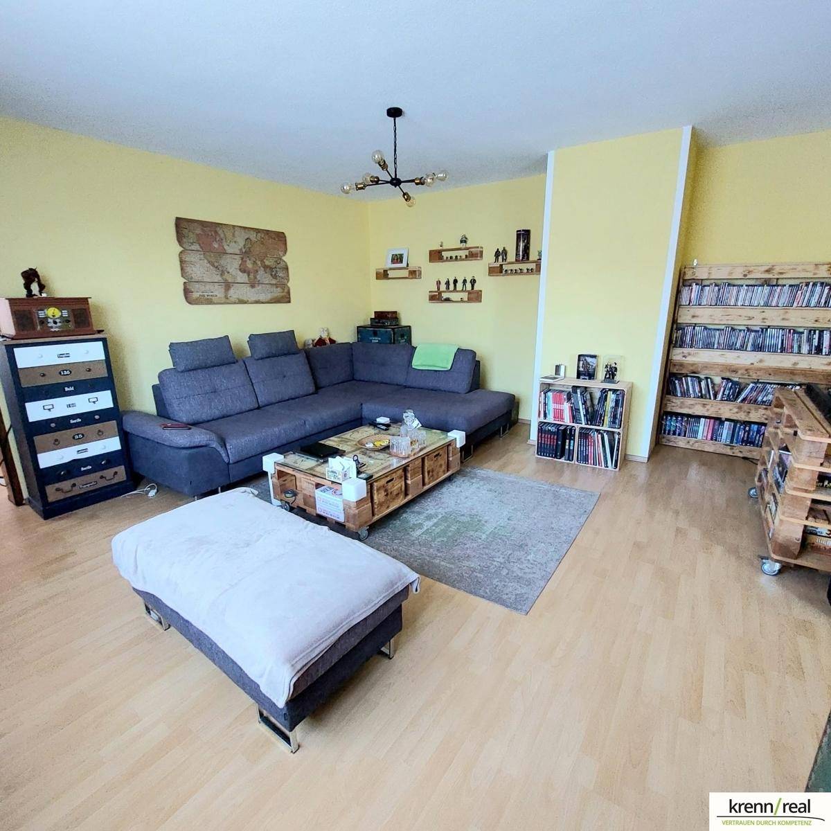 Helles Wohnzimmer mit großem Sofa, Laminatboden und gelben Wänden, dekoriert mit Büchern.