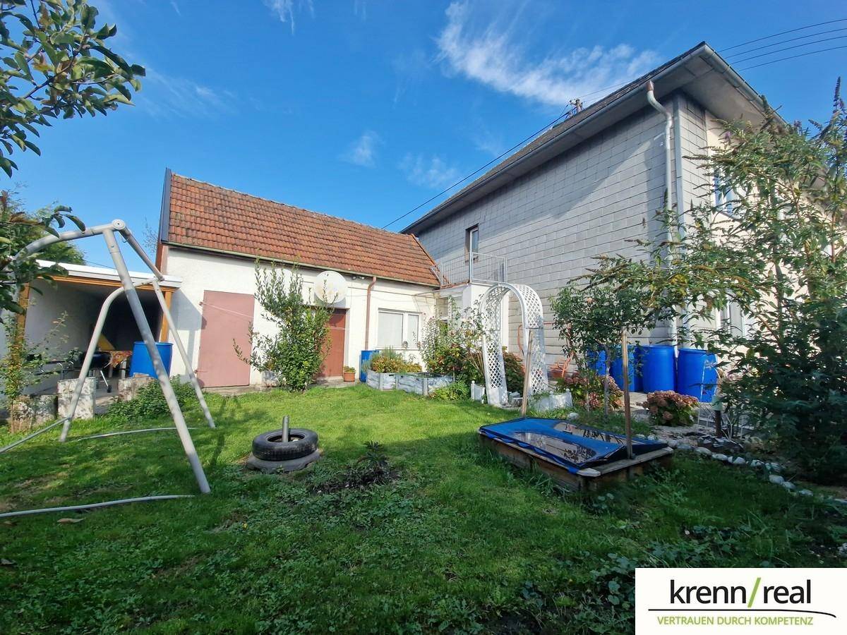 Weitläufiger Garten mit Schaukel, Sandkasten und blühenden Pflanzen neben dem Haus.