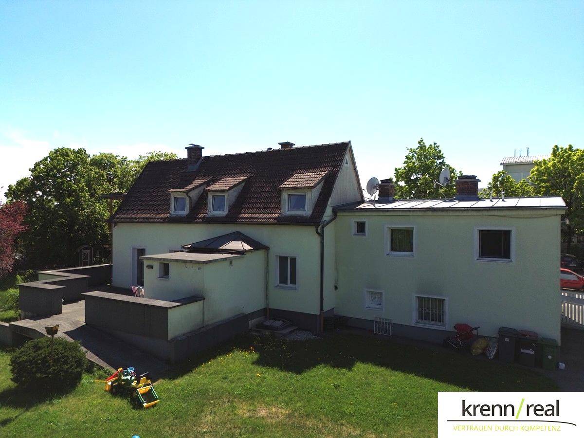 Seitenansicht des Hauses mit großem Rasenbereich und angrenzenden Terrassenstrukturen unter klarem Himmel.