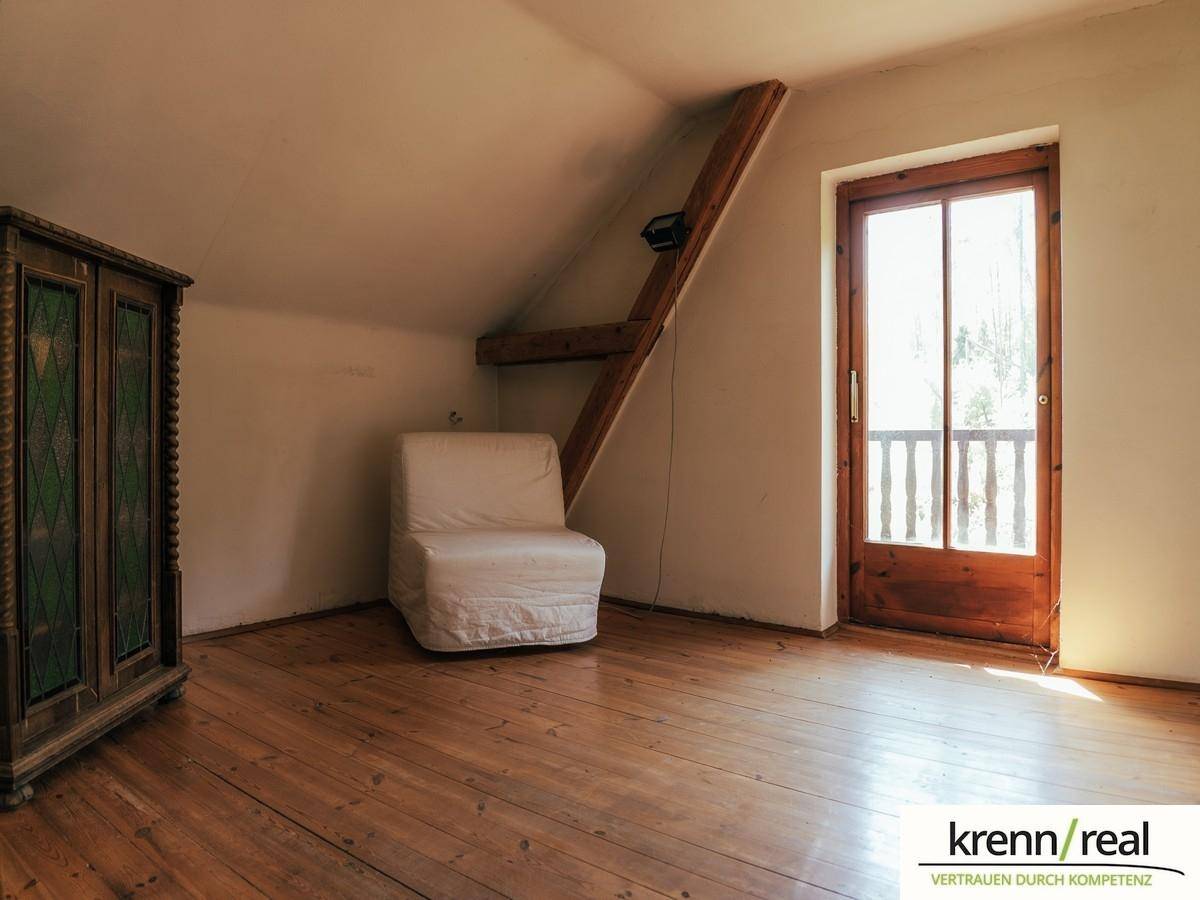 Helles Schlafzimmer im Dachgeschoss mit Holzboden, Schrank und Balkonzugang.