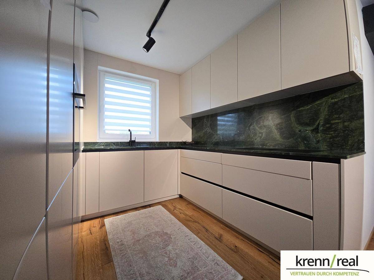 Moderne Küche mit hellen Schränken, dunkler Arbeitsplatte und Fenster.