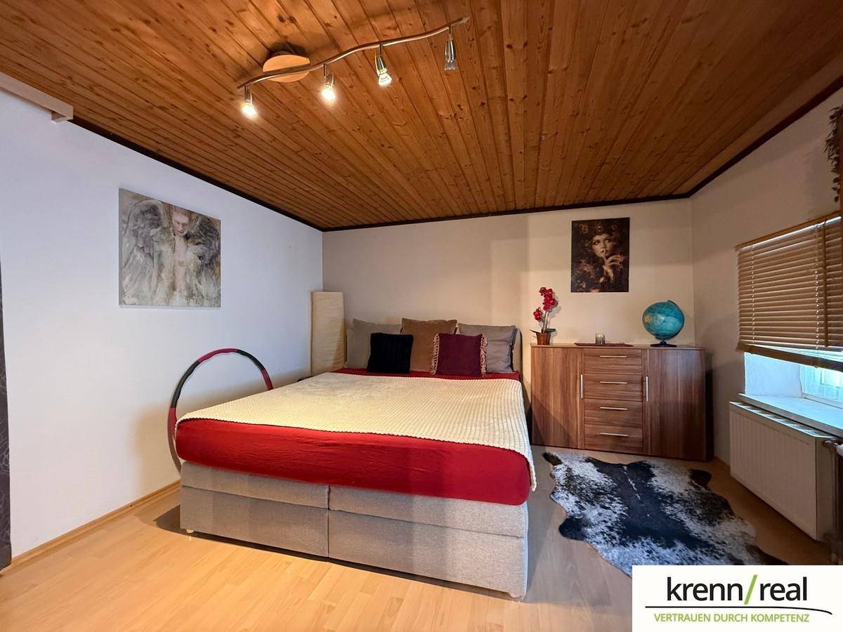 Helles Schlafzimmer mit Holzbalkendecke, Doppelbett und Fenster mit Blick nach draußen.