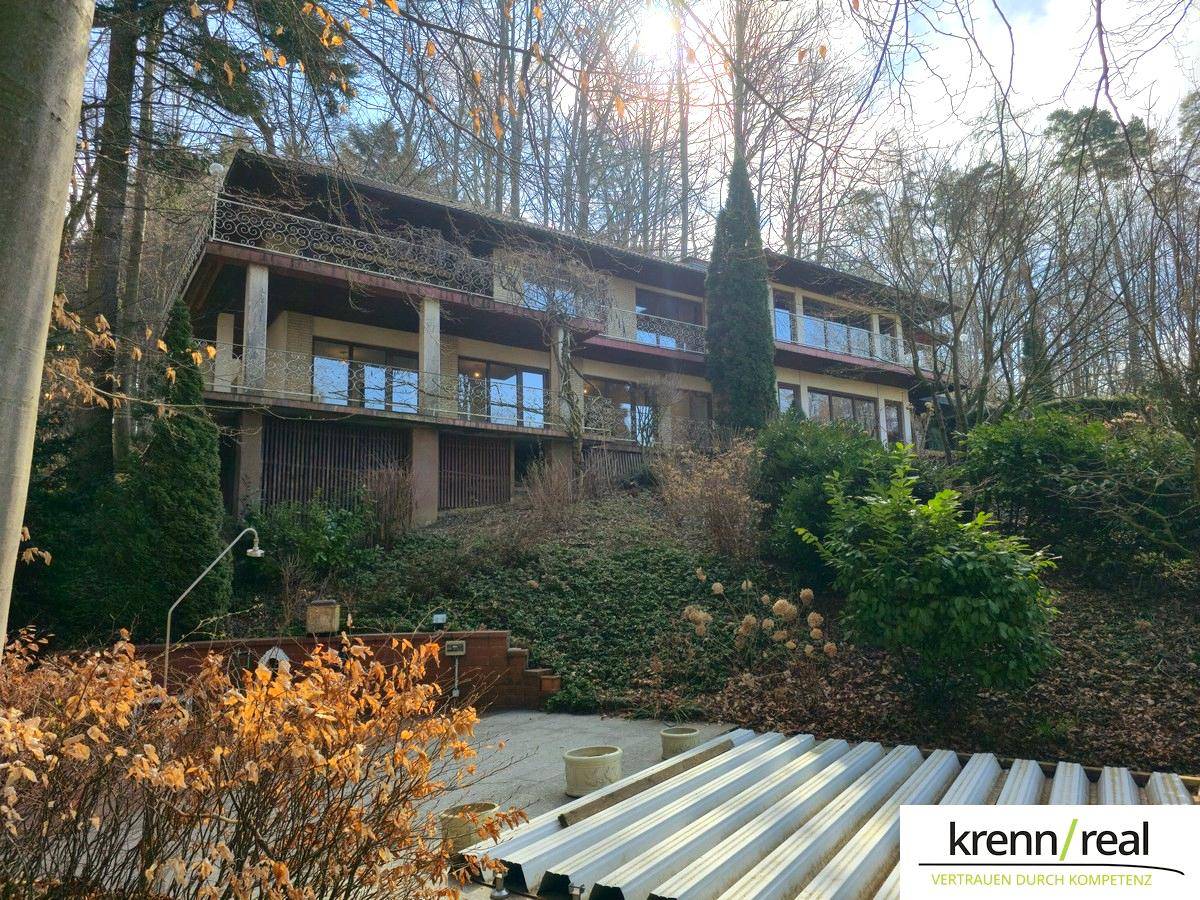 Seitenansicht des Hauses mit terrassiertem Gartenbereich und der Fassade, umgeben von Bäumen.