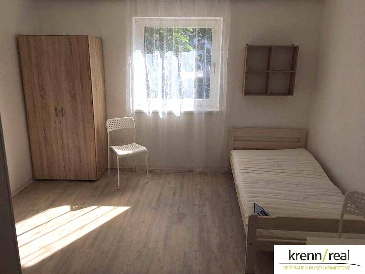 Helles Schlafzimmer mit Einzelbett, Kleiderschrank und Laminatboden, gut beleuchtet durch ein Fenster.