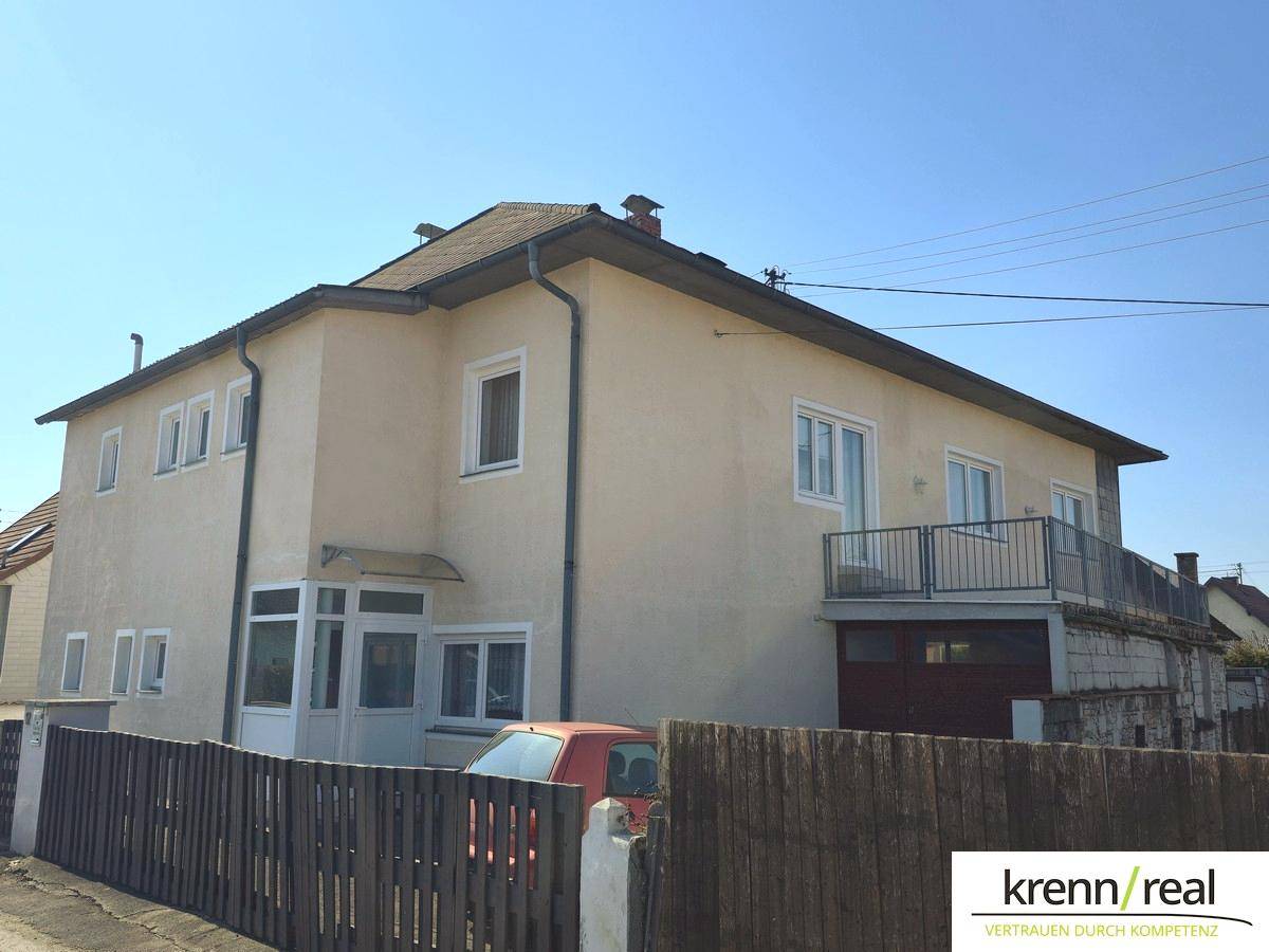 Rückansicht des Hauses mit Balkon und überdachtem Eingangsbereich unter strahlendem Sonnenschein.