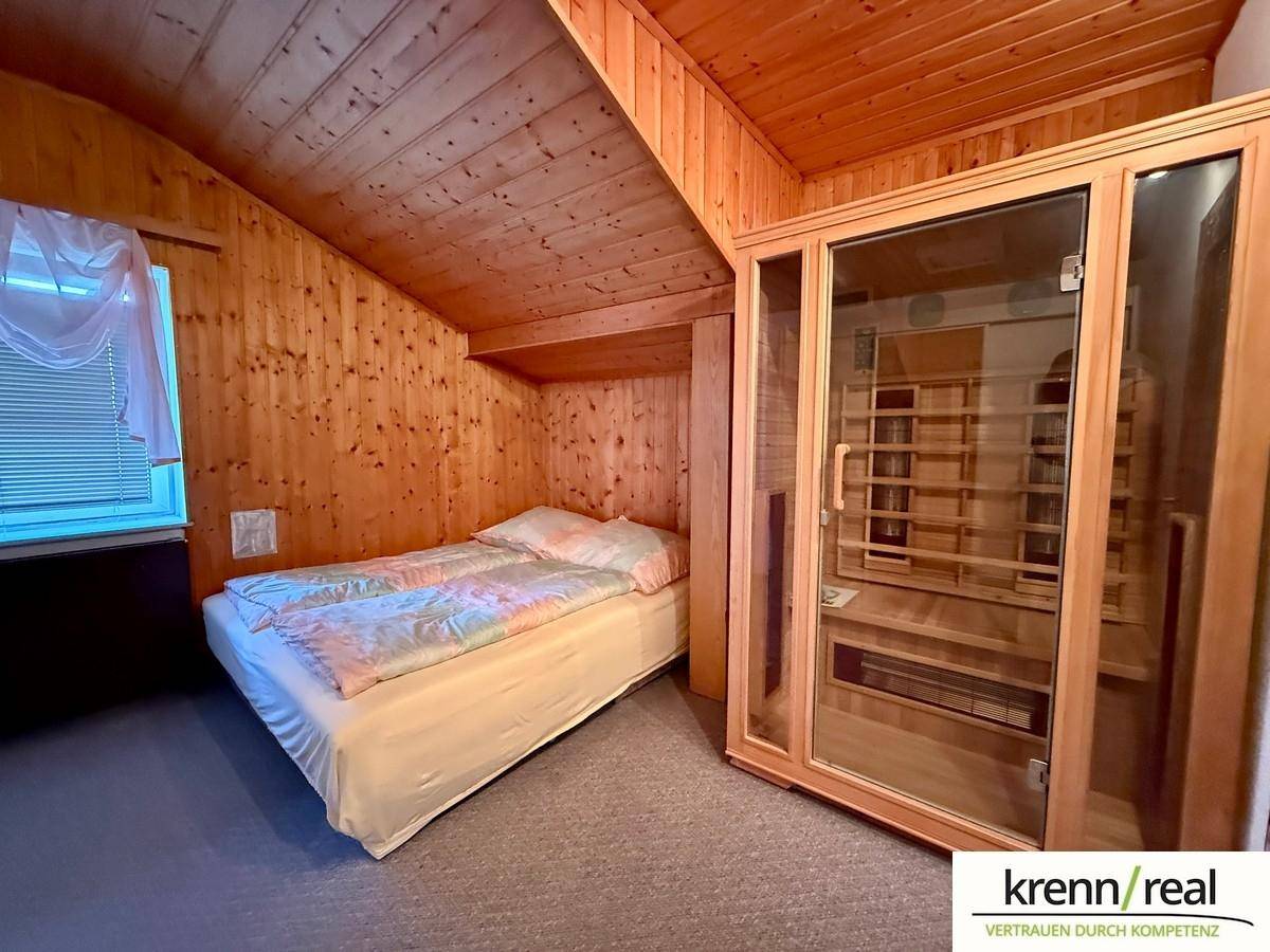 Gemütliches Schlafzimmer mit Holzverkleidung, Bett und einer integrierten Infrarotkabine.