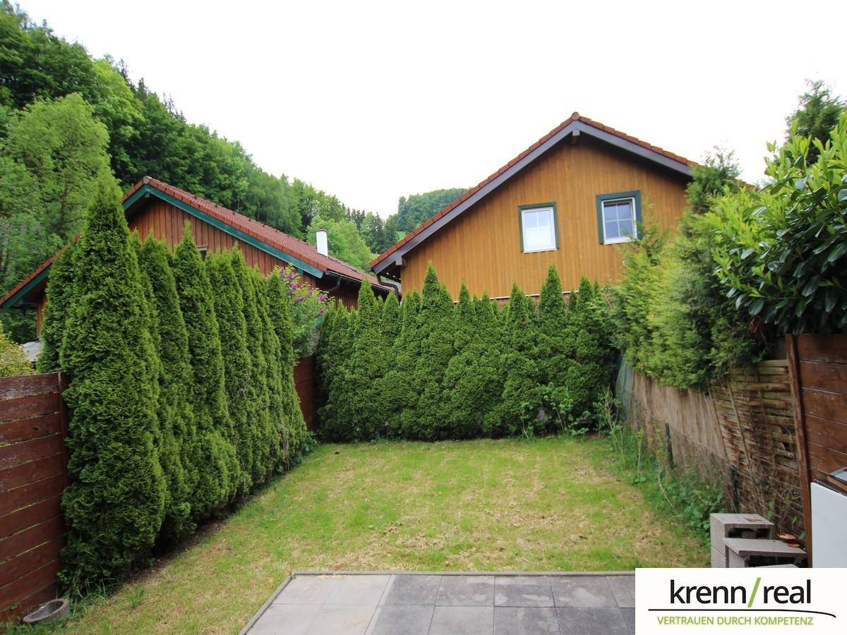Gepflegter Gartenbereich mit Rasenfläche, gepflasterter Terrasse und hohen Hecken für Privatsphäre.