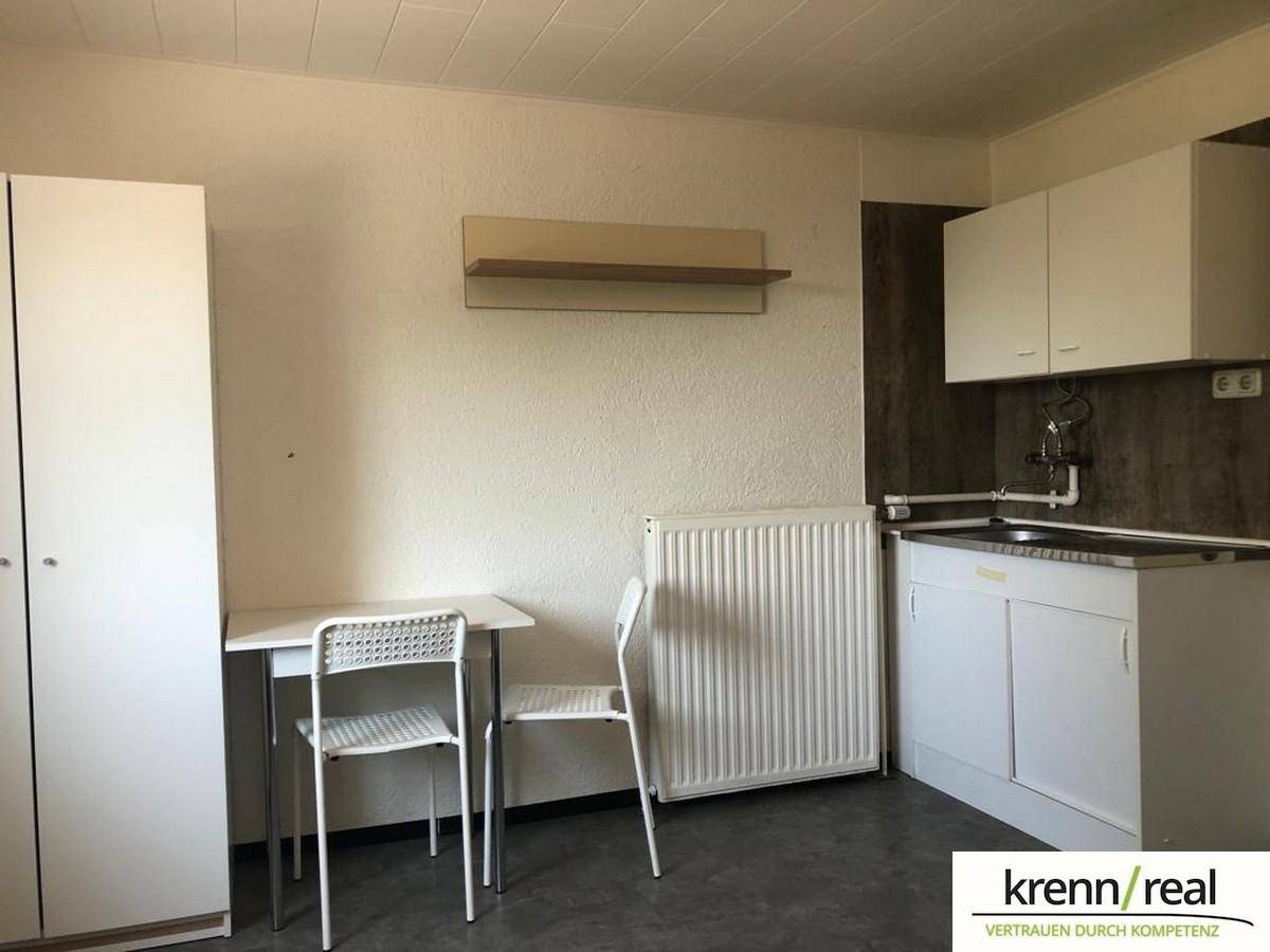 Kleiner Wohnbereich mit Küchenzeile, Heizkörper, Tisch und Stühlen, ideal für ein Studio-Apartment.