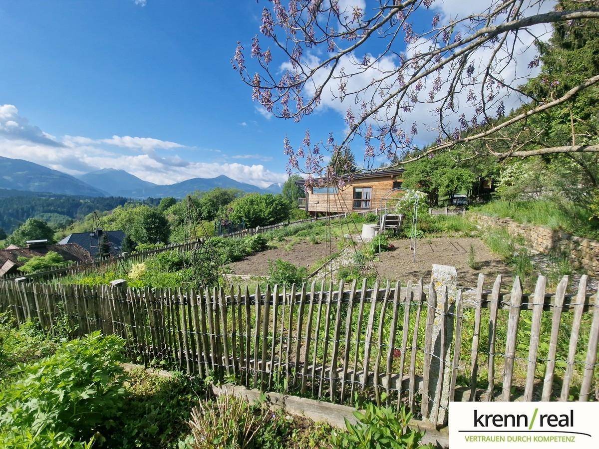 Gepflegter Gartenbereich mit Holzzaun und Blick auf ein charmantes Holzhaus sowie die umliegende Berglandschaft.