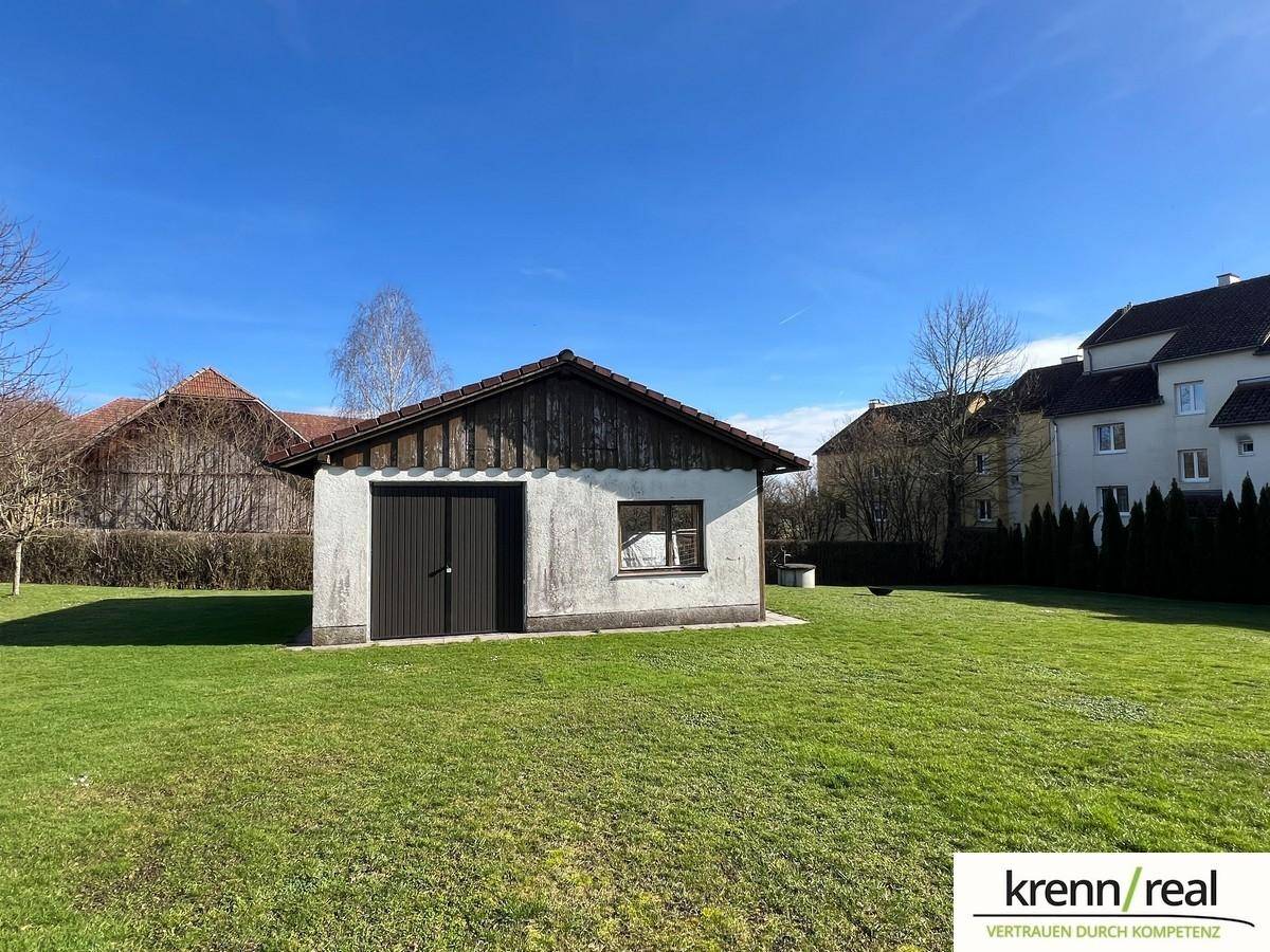 Freistehende Garage oder Schuppen auf einer grünen Wiese mit ländlicher Umgebung.