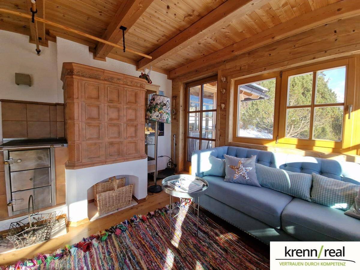 Rustikales Wohnzimmer mit Kachelofen, Holzbalkendecke und bequemer blauer Couch.