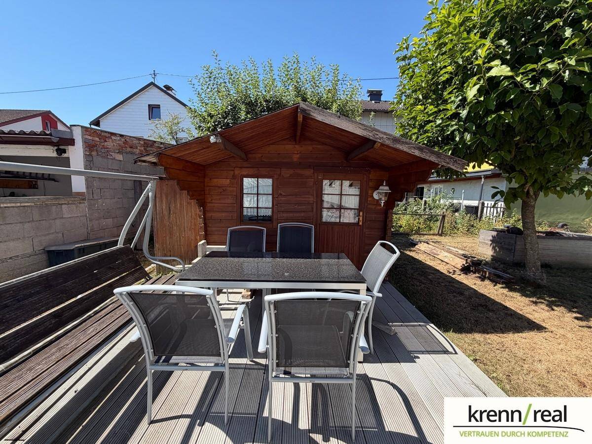 Gemütlicher Außenbereich mit Holzterrasse, Gartenmöbeln und einem kleinen Gartenhaus.