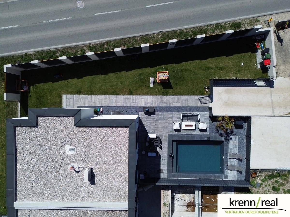 Luftaufnahme des Anwesens mit Flachdach, Pool, Garten und angrenzender Straße.
