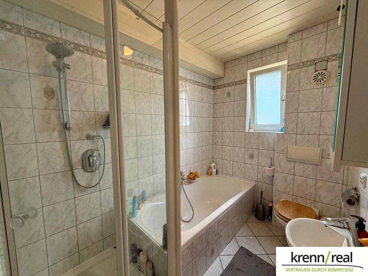 Gefliestes Badezimmer mit Badewanne, separater Dusche, Waschbecken und Fenster.