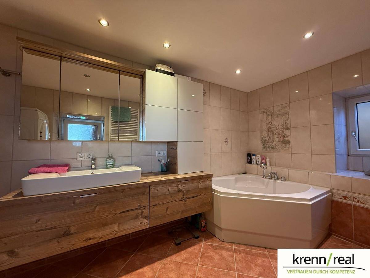 Geräumiges Badezimmer mit Eckbadewanne, modernem Waschtisch und Fliesen an Wänden und Boden.