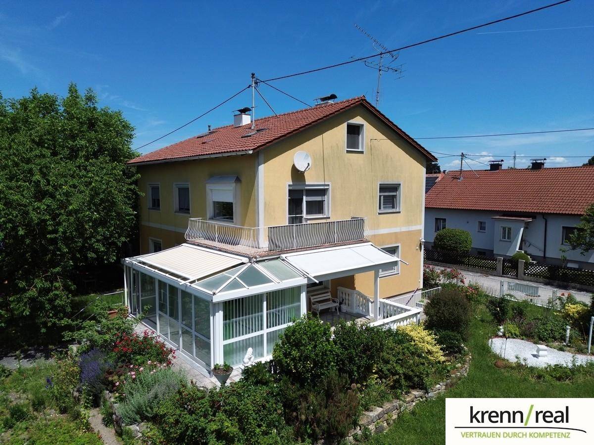 Rückansicht des Hauses mit gelber Fassade, Balkon und einem verglasten Wintergarten im Erdgeschoss.