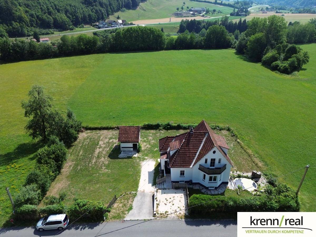 Weitläufige Luftaufnahme des Hauses mit umliegenden Feldern und bewaldeten Hügeln.