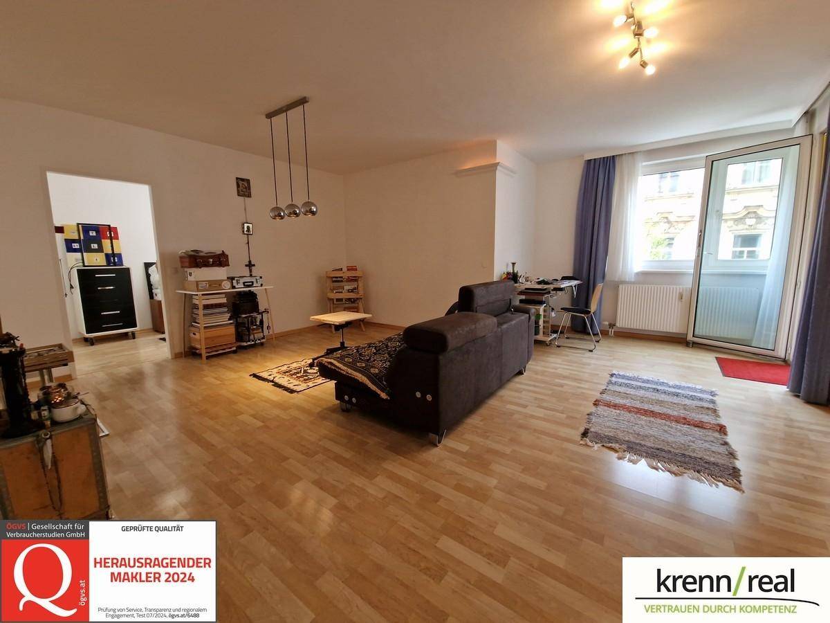 Helles Wohnzimmer mit Parkettboden, Sofa und Zugang zu einem kleinen Balkon.