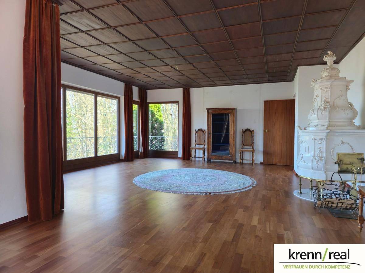Geräumiges Wohnzimmer mit Holzboden, Kassettendecke und einem eleganten Kachelofen.
