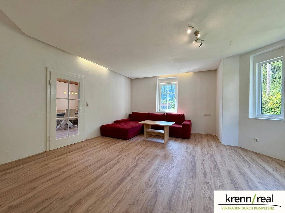 Helles Wohnzimmer mit Laminatboden, rotem Sofa und Blick auf die Natur.