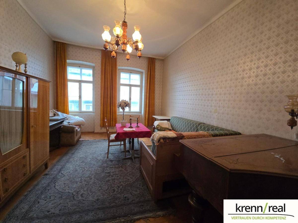 Traditionell eingerichtetes Zimmer mit gemusterter Tapete, Kronleuchter und antiken Möbeln.