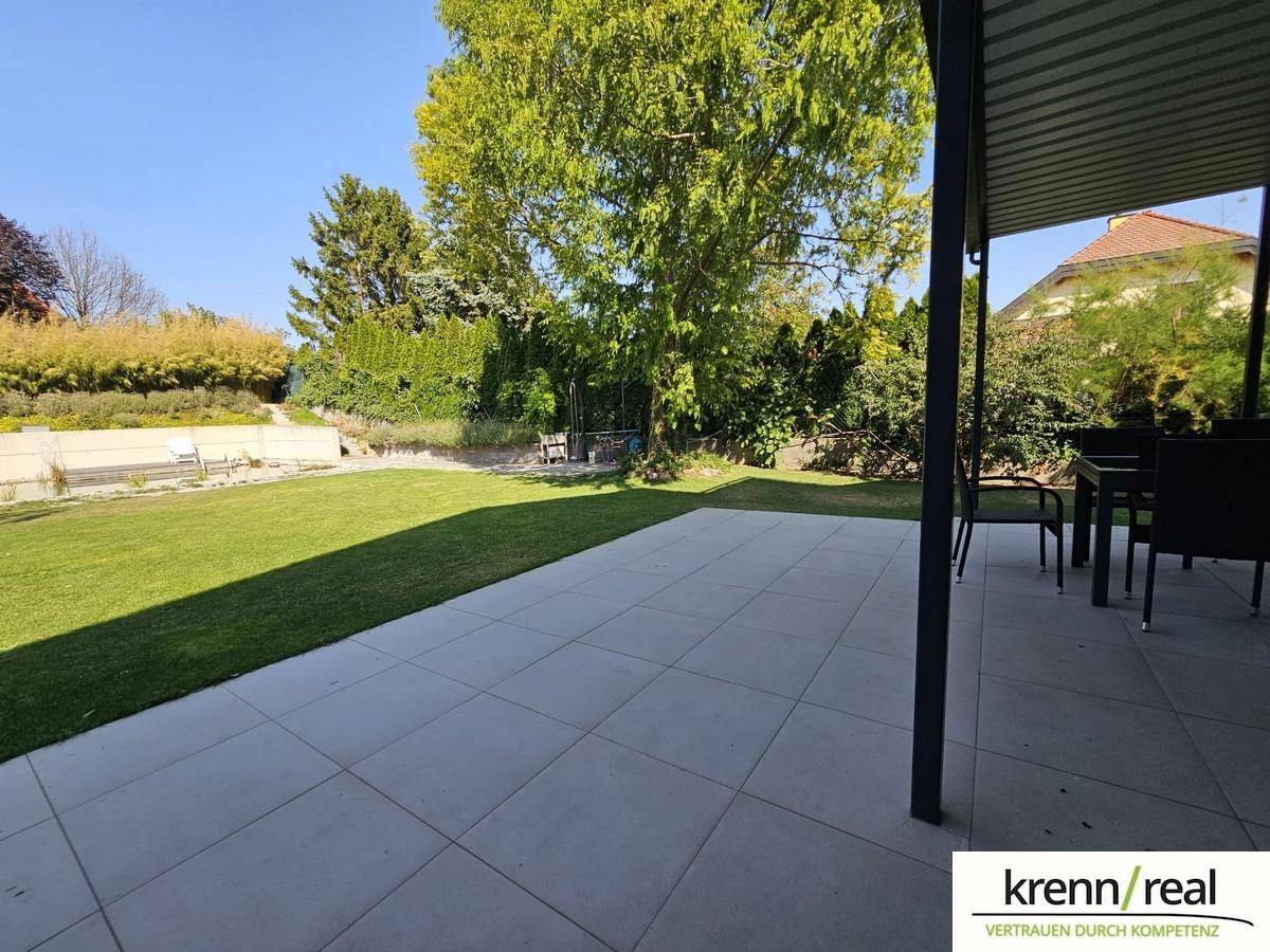 Geräumige, geflieste Terrasse mit Gartenmöbeln und weitem Blick in den grünen Garten.