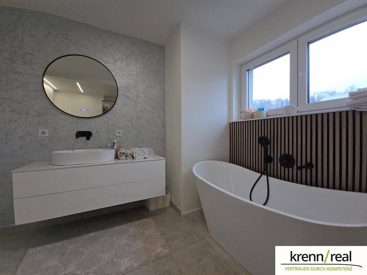 Modernes Badezimmer mit freistehender Badewanne, Einzelwaschbecken und Fenster.