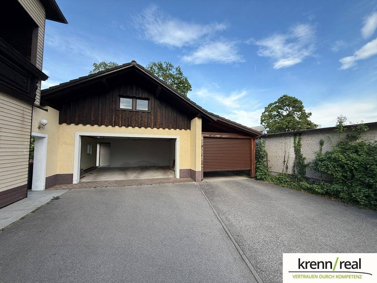 Außenansicht einer Doppelgarage mit Carport und Zufahrt unter blauem Himmel.