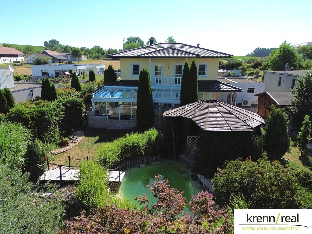 Gesamtaufnahme des Hauses mit großem Garten, Teich und Pavillon in ländlicher Umgebung.