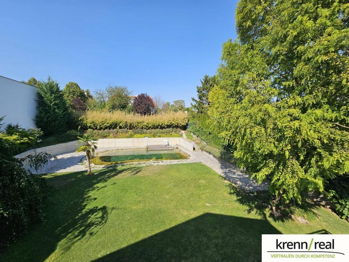 Weitläufiger Garten mit großem Naturteich und üppiger Bepflanzung unter blauem Himmel.