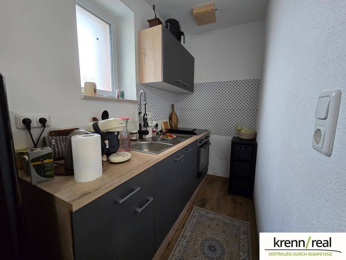 Kompakte Küche mit dunklen Schränken, Holz-Arbeitsplatte, integriertem Ofen und Fenster.