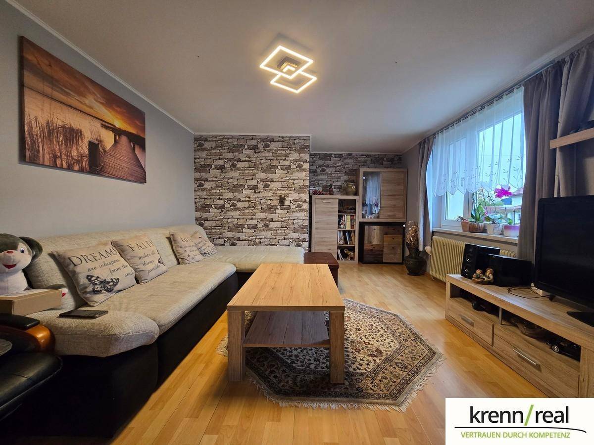 Gemütliches Wohnzimmer mit bequemer Couch, Holzboden und einer Akzentwand in Steinoptik.