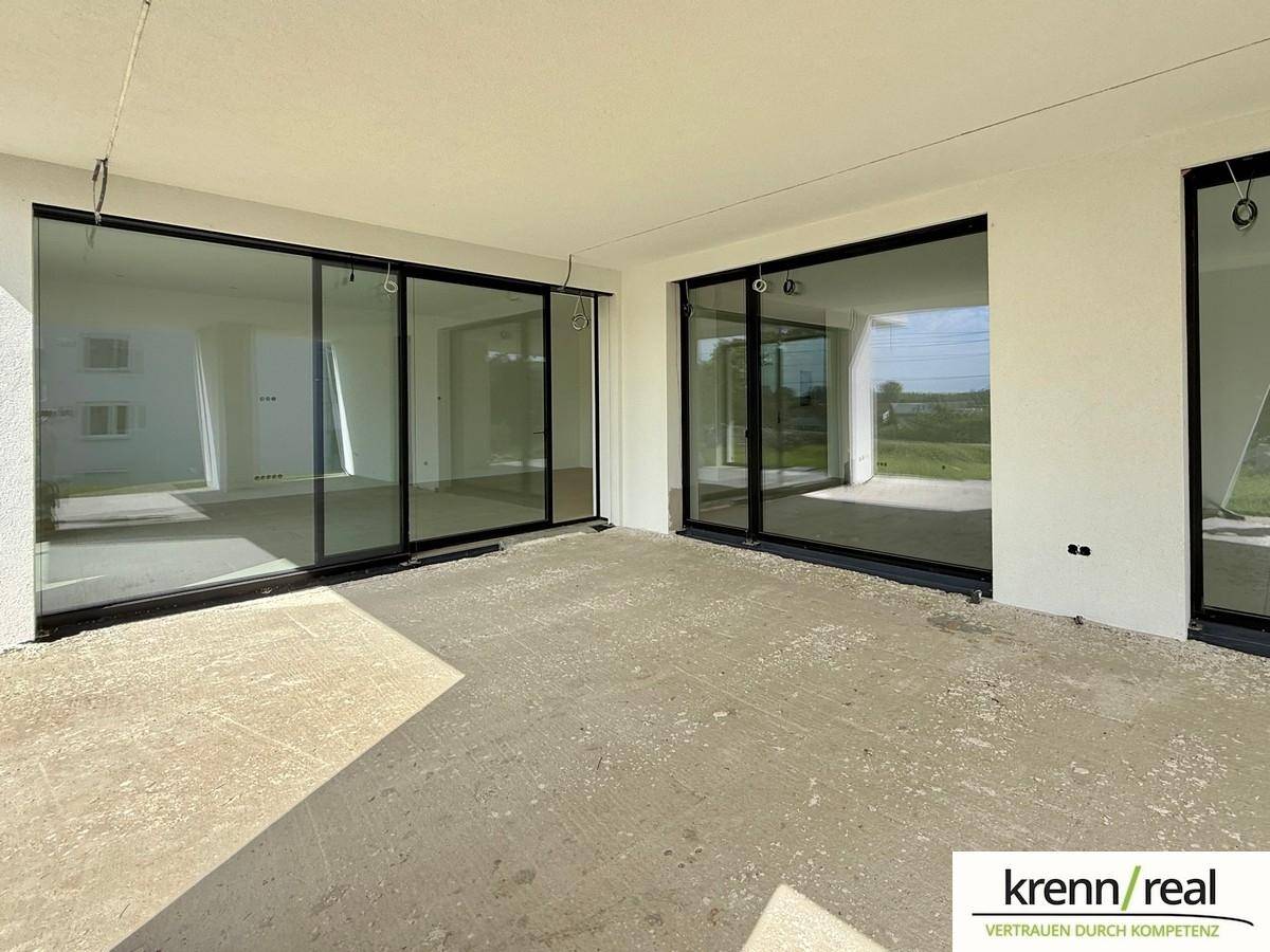 Überdachte Terrasse mit Betonboden und großen Glasschiebetüren, die den Zugang zum Innenbereich ermöglichen.
