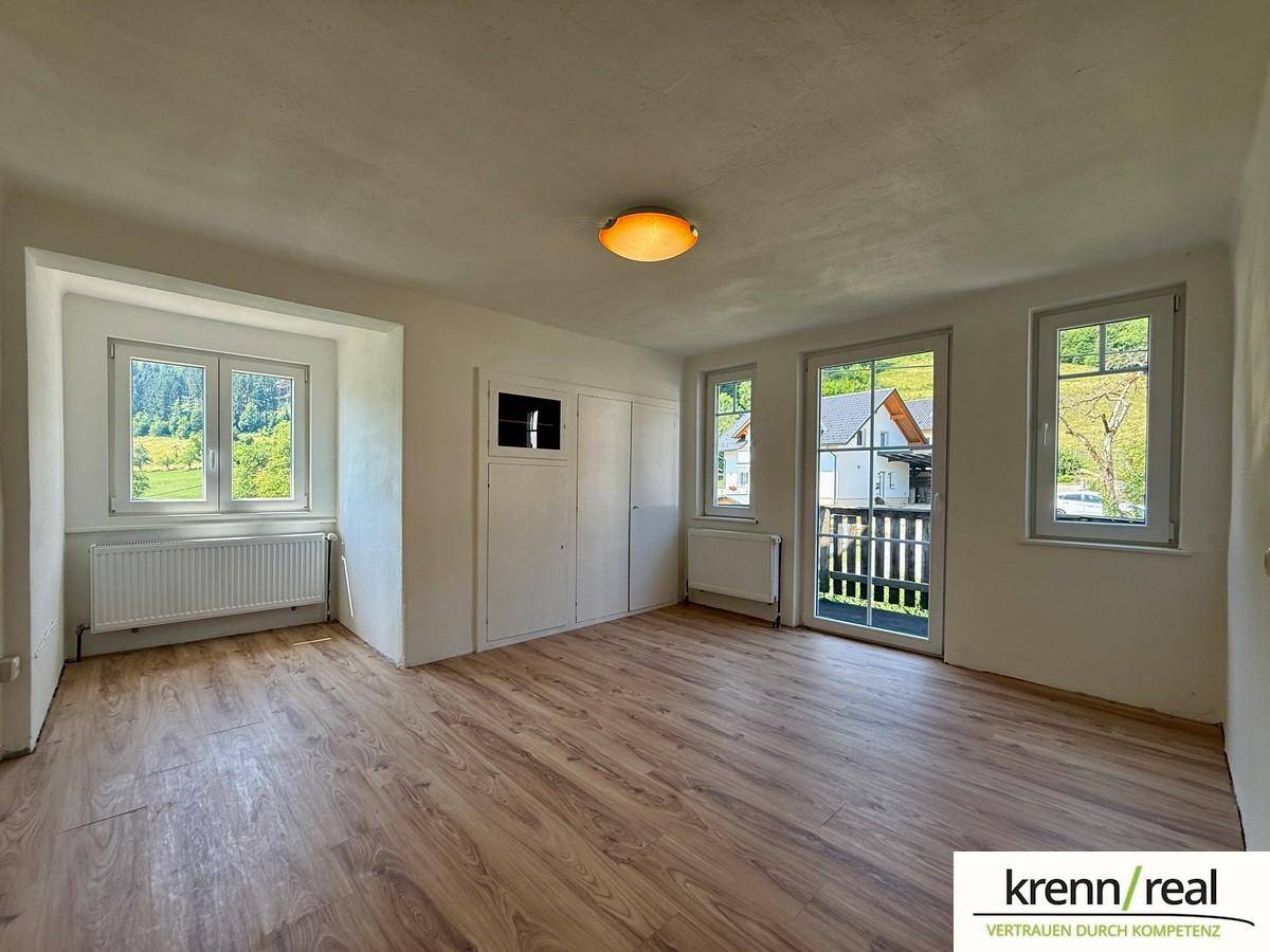 Helles Zimmer mit Laminatboden, Einbauschrank und Zugang zu einem Balkon mit Blick auf die Umgebung.