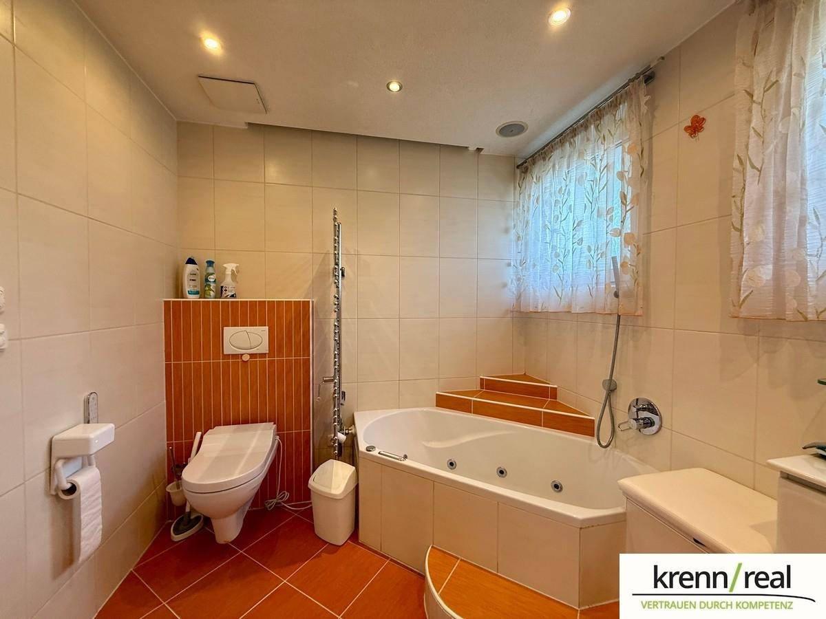 Gefliestes Badezimmer mit Eckbadewanne, Toilette und einem kleinen Fenster für natürliche Belüftung.