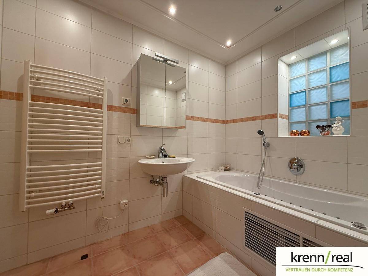 Gefliestes Badezimmer mit Badewanne, Einzelwaschbecken, beheiztem Handtuchhalter und Glasbausteinfenster.