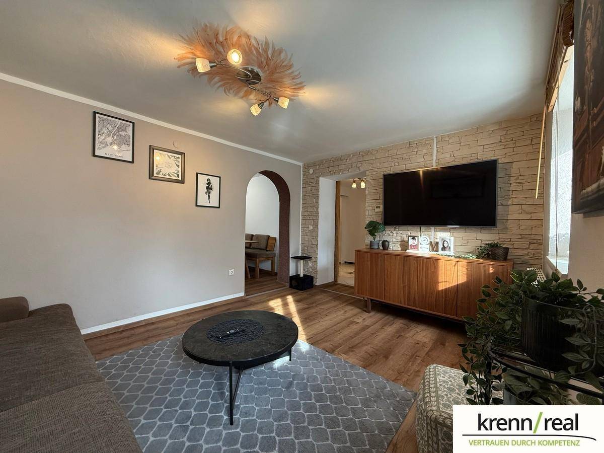 Gemütliches Wohnzimmer mit Sofa, Couchtisch und einer dekorativen Steinwand, die zum Essbereich führt.