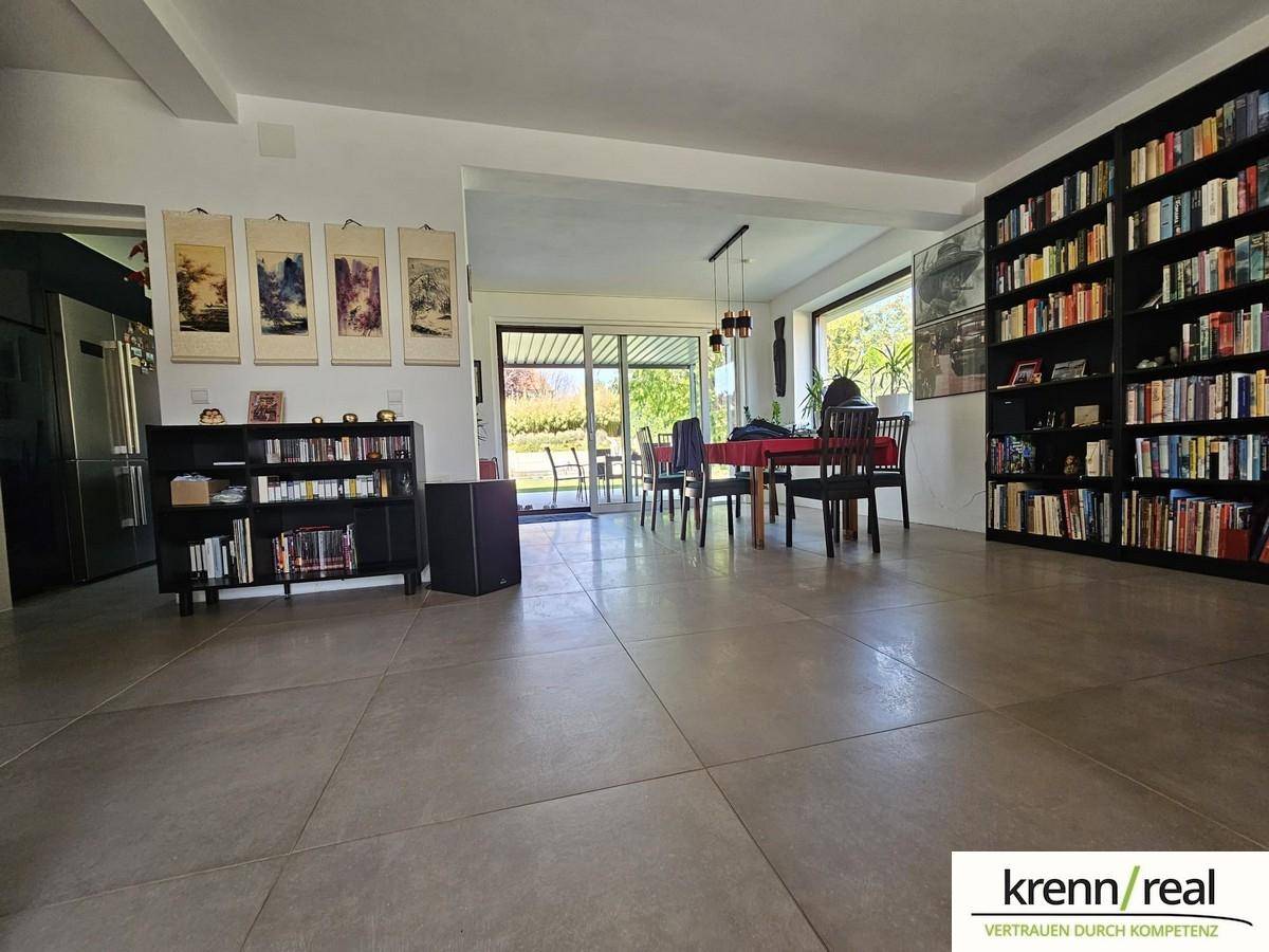 Offener Wohn- und Essbereich mit großem Bücherregal, Fliesenboden und Zugang zur Terrasse.