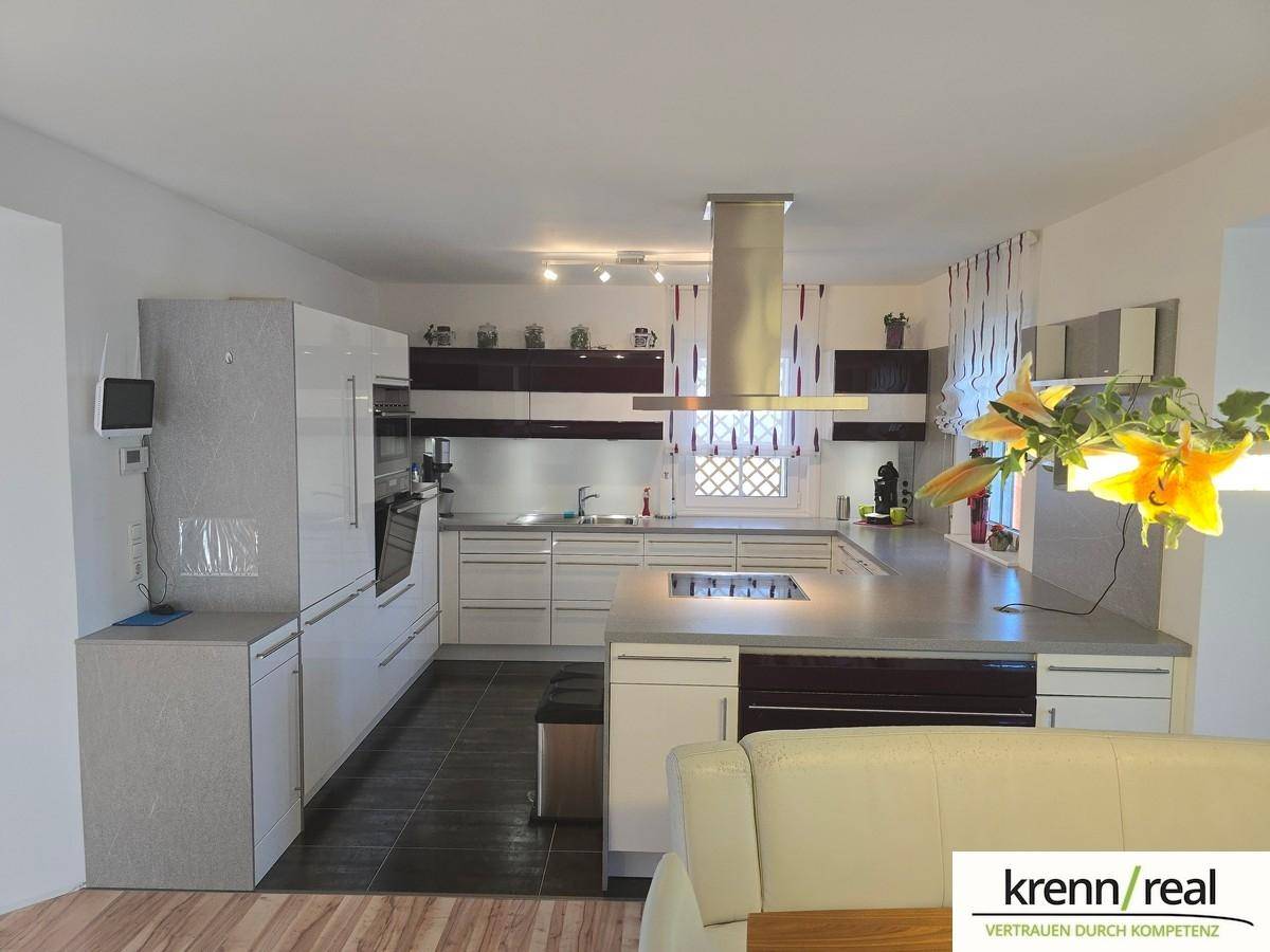 Moderne Küche mit weißen Hochglanzfronten, Kochinsel und integrierten Geräten.