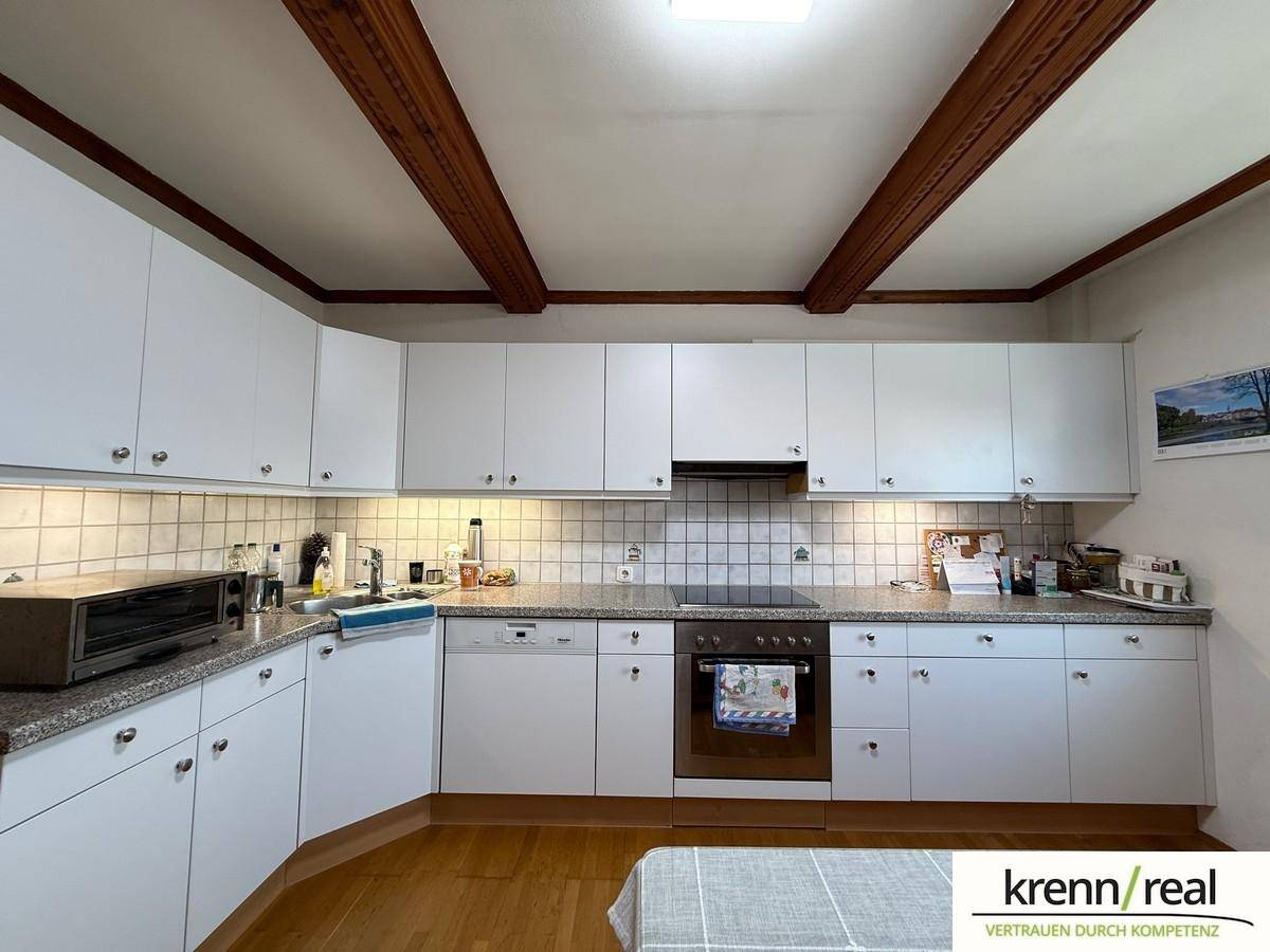 Klassische Küche mit weißen Schränken, gefliestem Spritzschutz und sichtbaren Holzbalken an der Decke.