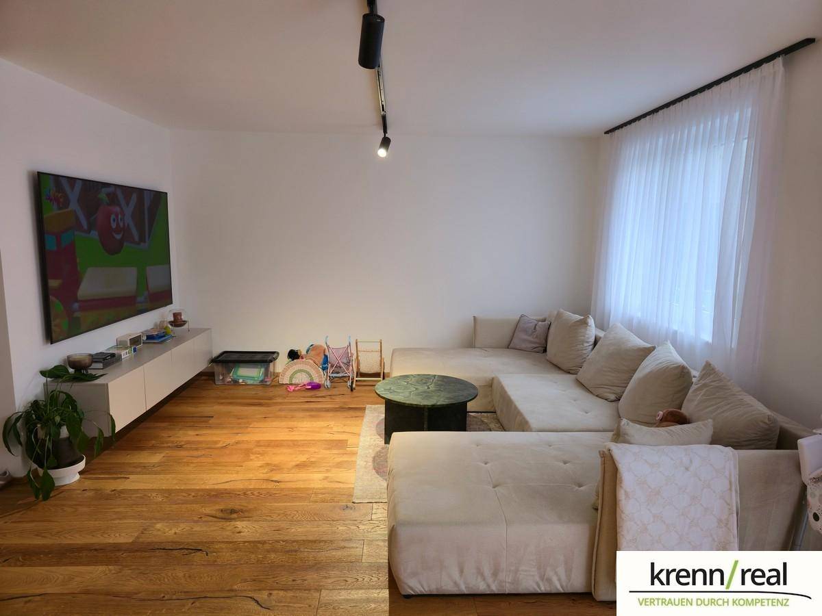 Gemütliches Wohnzimmer mit großem Sofa, Holzboden und viel Tageslicht.