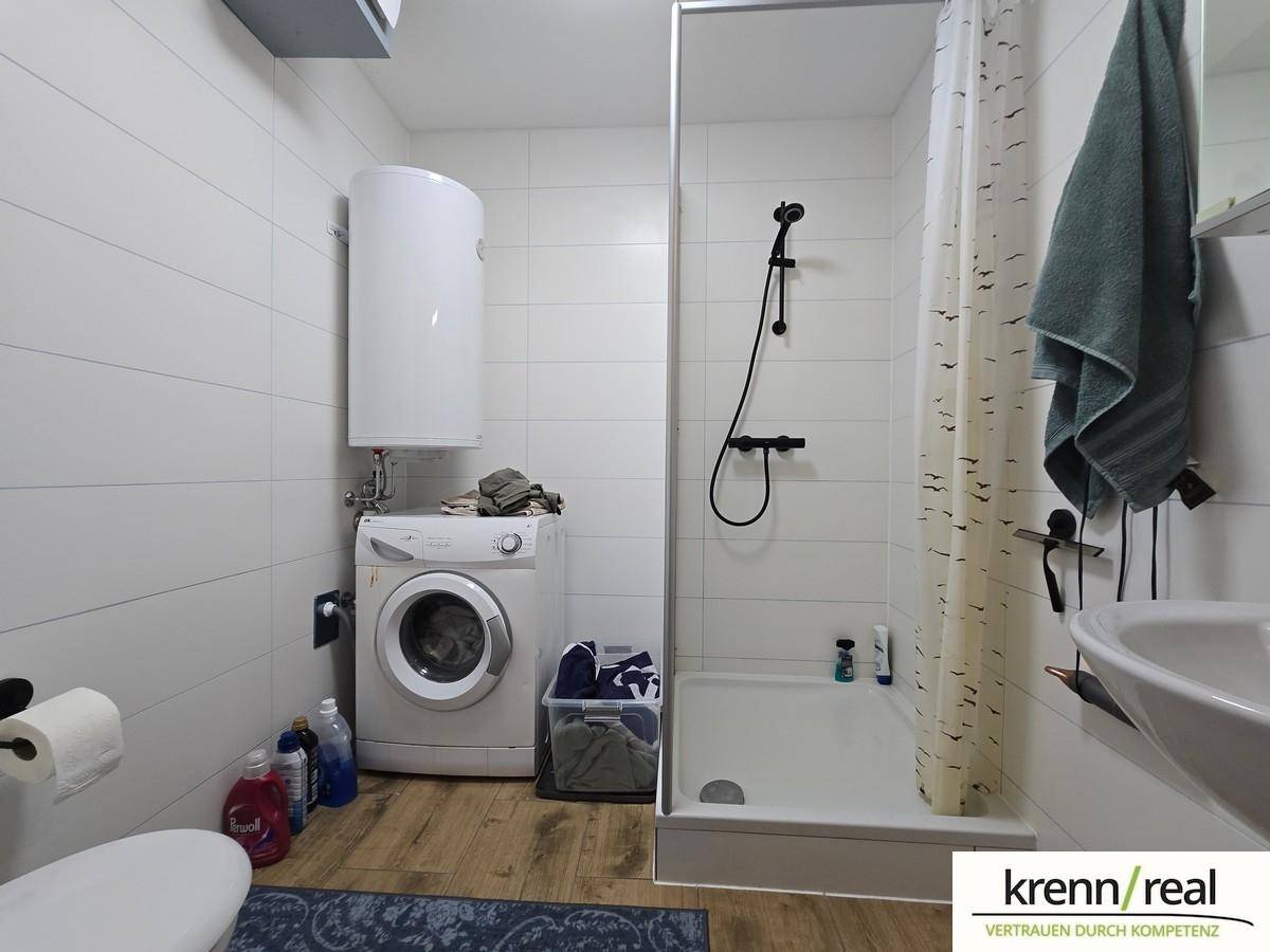 Modernes Badezimmer mit Duschkabine, Waschmaschine und weißen Fliesen an den Wänden.